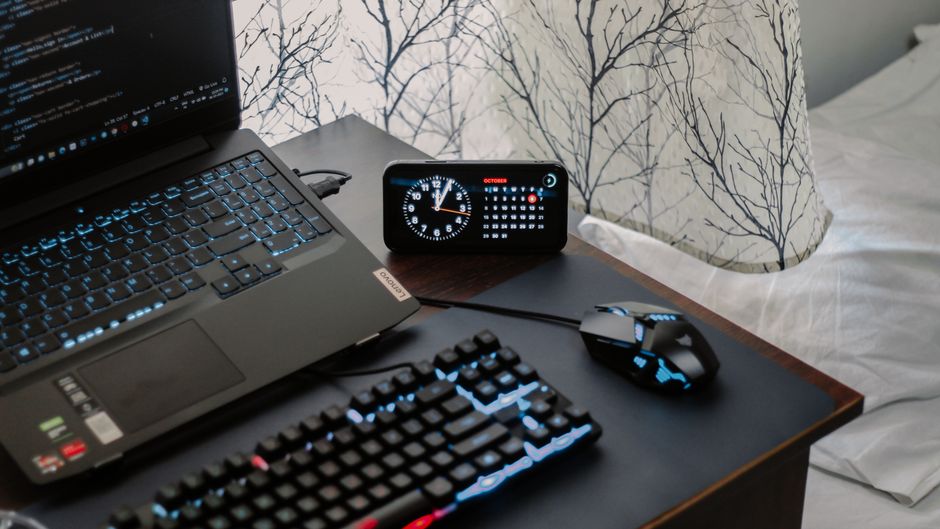 A modern workspace featuring a laptop, digital clock, gaming mouse, and keyboard.